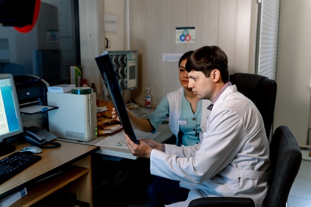 Médico radiologista masculino sentado com uma colega de escritório. Discutindo filme de ressonância magnética. Problemas medicos.