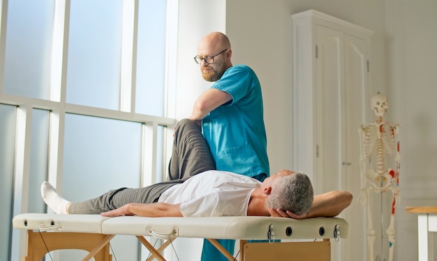 Un médico realiza una sesión de fisioterapia después de un trauma médico con un hombre en la rehabilitación moderna ...