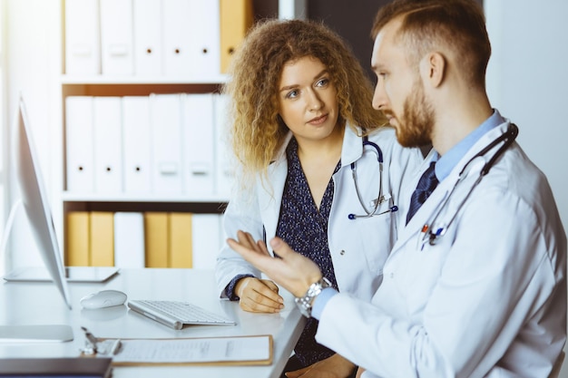 Médico ruivo com colega discutindo a terapia da doença atual enquanto está sentado no local de trabalho na clínica ensolarada Trabalho em equipe em medicina