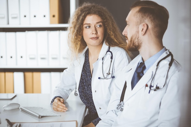 Médico ruivo com colega discutindo a terapia da doença atual enquanto está sentado no local de trabalho na clínica. Trabalho em equipe na medicina.