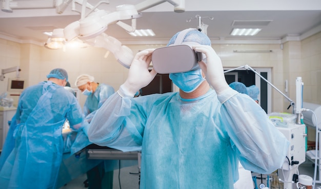 Médico en una sala quirúrgica con gafas de realidad virtual en el fondo de la operación real.