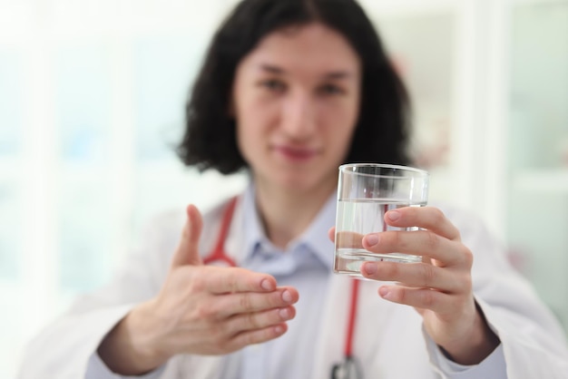 Médico satisfecho sosteniendo un vaso de agua limpia en la mano mira a la cámara hombre de pelo largo recomienda