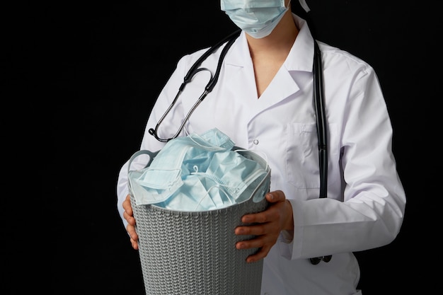 Médico segurando um balde cheio de máscaras faciais usadas, jogando-as fora como símbolo do fim da epidemia