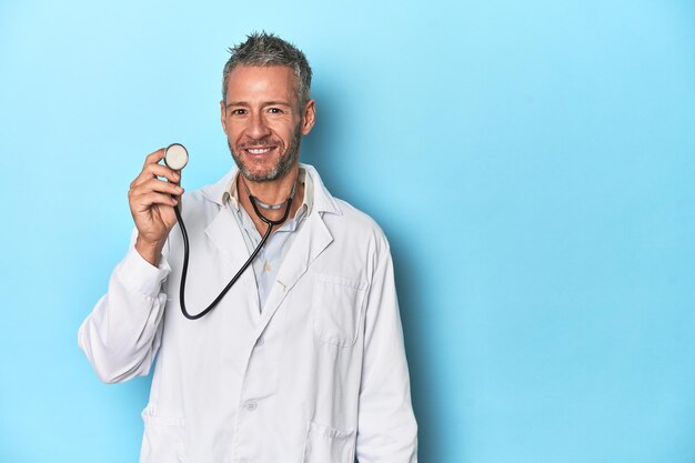 Médico segurando um estetoscópio no pano de fundo azul do estúdio