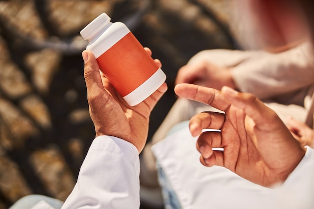 Médico segurando um recipiente de remédio branco e laranja na mão enquanto aponta para ele