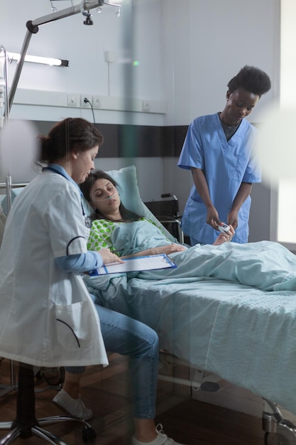 Foto el médico señala los resultados de laboratorio en el portapapeles explicando el diagnóstico al paciente en la cama del hospital mientras la enfermera pone el oxímetro de pulso en el dedo. mujer que se siente enferma siendo consultada por trabajadores de la salud.