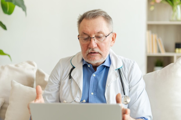 Médico sênior com laptop fala em videoconferência tem consulta com o paciente profissional sênior