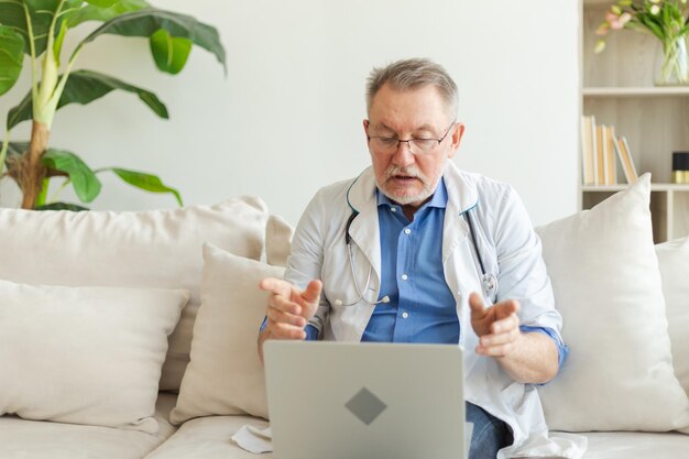 Un médico senior con una computadora portátil habla en una videollamada y tiene una consulta con un paciente profesional senior