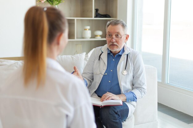 Médico senior examinando a una mujer joven en el consultorio médico o en casa, la paciente y el médico tienen estafa