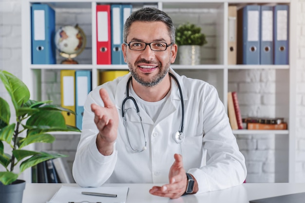 Médico senior hablando con la cámara en video chat desde su oficina