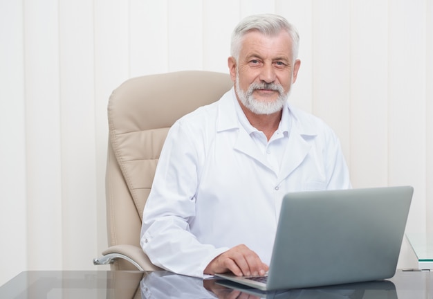 Médico senior inteligente trabajando en la computadora portátil en la oficina.