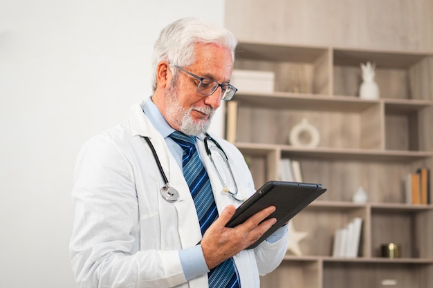 Médico sênior maduro em uniforme médico usando tablet digital em clínica terapeuta profissional
