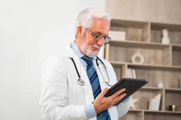 Médico sênior maduro em uniforme médico usando tablet digital em clínica terapeuta profissional