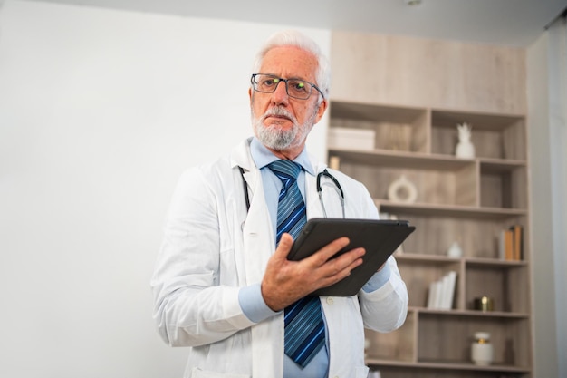 Médico sênior maduro em uniforme médico usando tablet digital em clínica terapeuta profissional