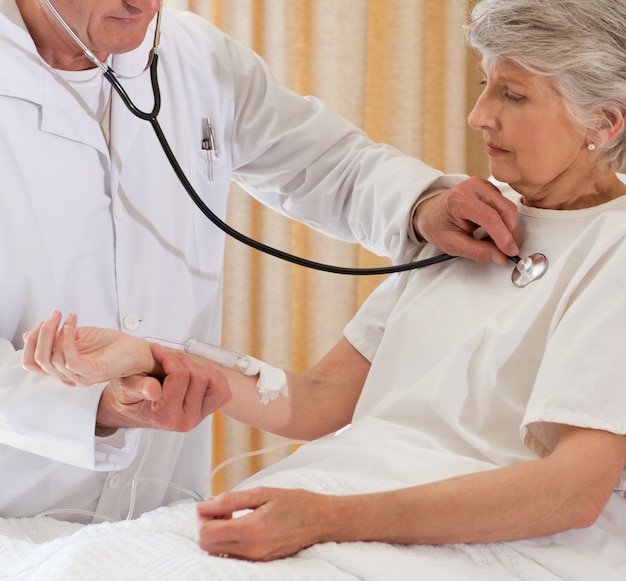 Médico sênior que toma os batimentos cardíacos de seu paciente