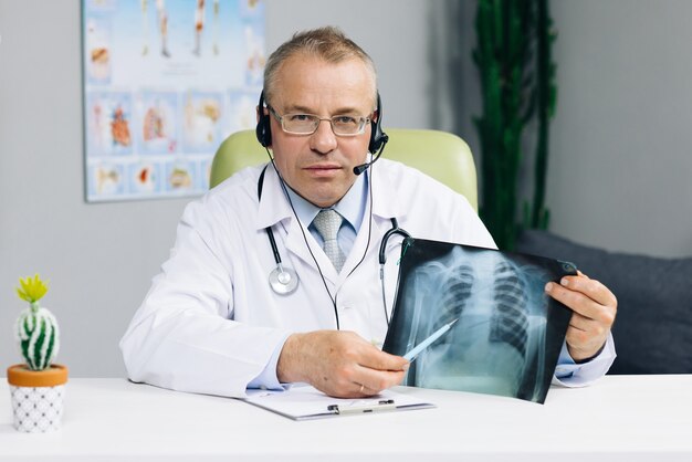 Médico sênior usando fone de ouvido, videoconferência sobre pandemia de vírus corona durante videoconferência em grupo, videochamada com webcam