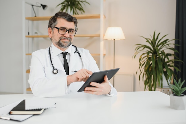 Médico sênior usando seu computador tablet no trabalho