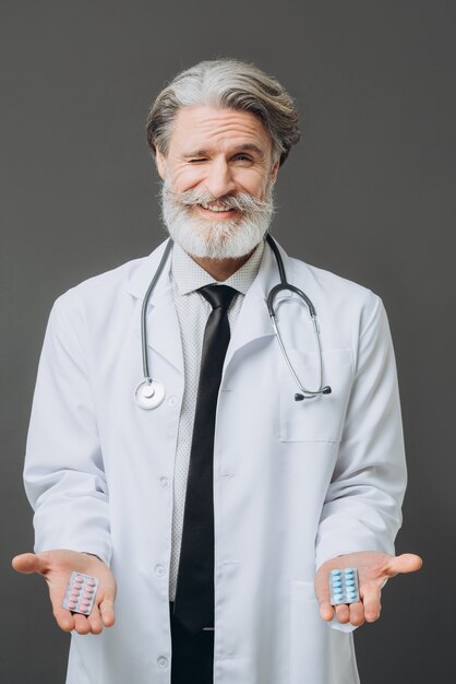 Médico señor barbudo dando pastillas en la pared gris