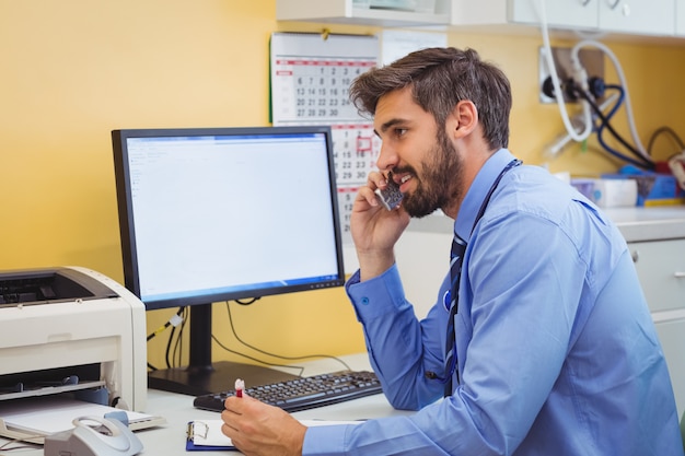 Médico sentado em sua mesa e falando no telefone