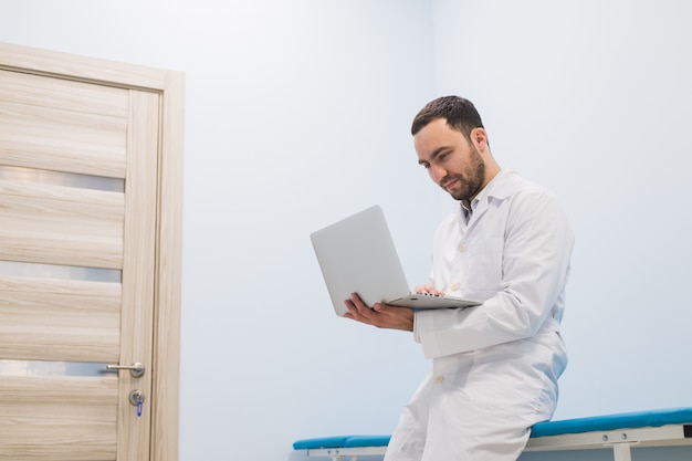 Médico sentado em uma cama de hospital com seu laptop