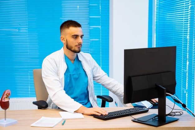 Médico serio que trabaja en una computadora en una clínica moderna El médico está trabajando en la oficina Médico experimentado en matorrales en la clínica Primer plano