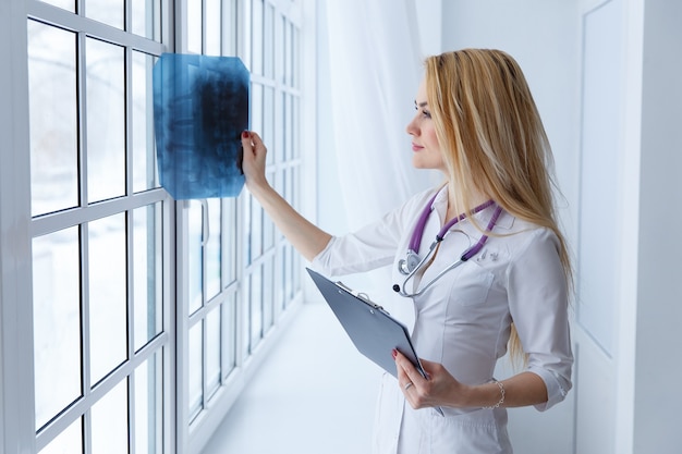 Médico de sexo femenino profesional joven que examina la radiografía del paciente de la columna vertebral humana durante una visita.