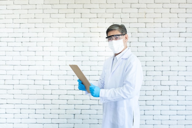 Foto un médico de sexo masculino asiático usa anteojos transparentes y una mano de mascarilla que sostiene un historial médico en un hospital.