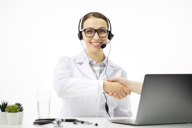 Foto médico sexy e inteligente con auriculares ofrece consulta en línea para el paciente en la computadora