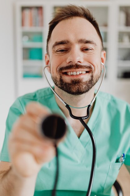 Médico sorridente com seu estetoscópio olhando para a câmera no consultório médico