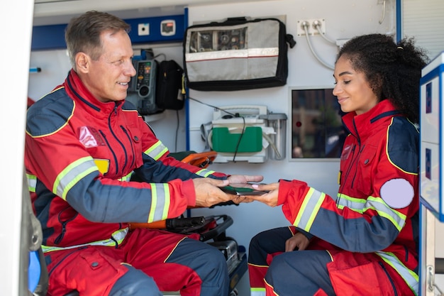 Foto médico sorridente dando o tablet para sua colega satisfeita no carro da ambulância