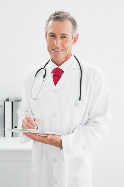 Foto médico sorridente que escreve um relatório no escritório