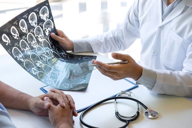 Médico sosteniendo y mirando una película de rayos X que examina el cerebro mediante una tomografía computarizada del paciente y analiza el resultado mientras discute la explicación del problema médico.