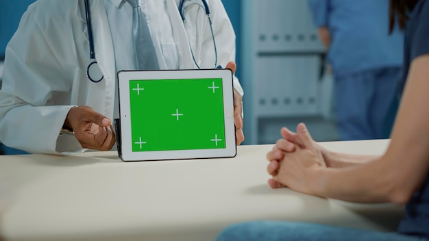 Médico sosteniendo una pantalla verde horizontal en una tableta digital en el gabinete. Médico general que utiliza una clave de croma en blanco con una plantilla de maqueta aislada y un fondo de espacio de copia en el dispositivo. De cerca