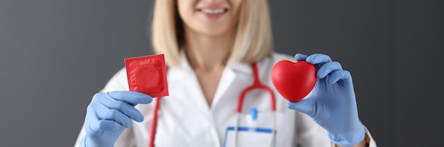 El médico sostiene el condón y el corazón rojo en su mano, la seguridad de la salud y el concepto de amor