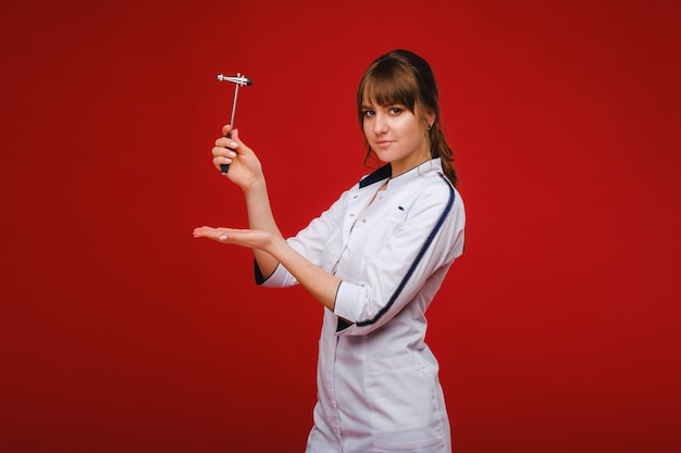 El médico sostiene un martillo neurológico sobre un fondo rojo. El neurólogo comprueba los reflejos del paciente con un martillo. Diagnóstico, salud y atención médica.