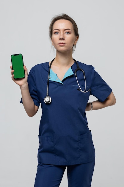 El médico sostiene un teléfono móvil con un cromakey Publicidad en un teléfono inteligente servicios médicos en una clínica