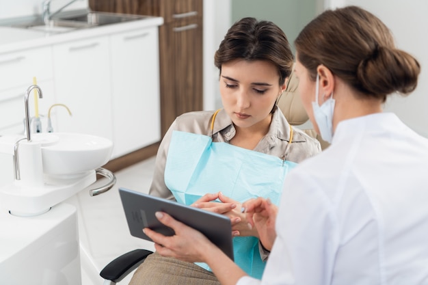 Foto un médico con su paciente en la oficina de odontología, usando una tableta