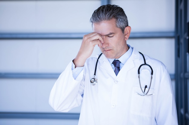 Médico tenso de pie con la mano en la frente en el hospital