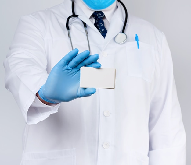 El médico terapeuta adulto está vestido con una túnica blanca uniforme y guantes estériles azules están de pie y sosteniendo una pila de tarjetas de visita de papel blanco vacías