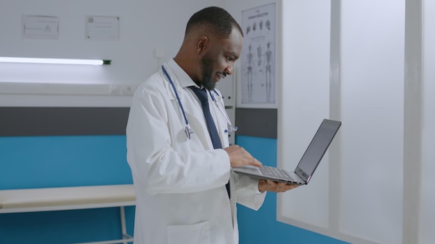 Médico terapeuta afroamericano parado en la oficina del hospital sosteniendo una tableta analizando la experiencia en enfermedades revisando el documento médico. Hombre médico que desarrolla un tratamiento de atención médica