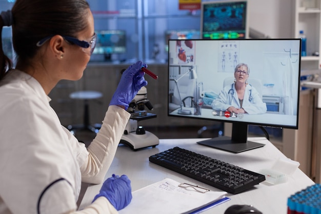 Médico terapeuta segurando tubos de ensaio discutindo experiência em sangue com químico remoto