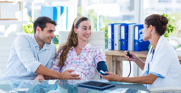 Médico tomando la presión arterial de una paciente embarazada con su esposo