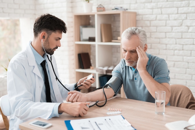 Médico con tonómetro mide la presión sanguínea del anciano.