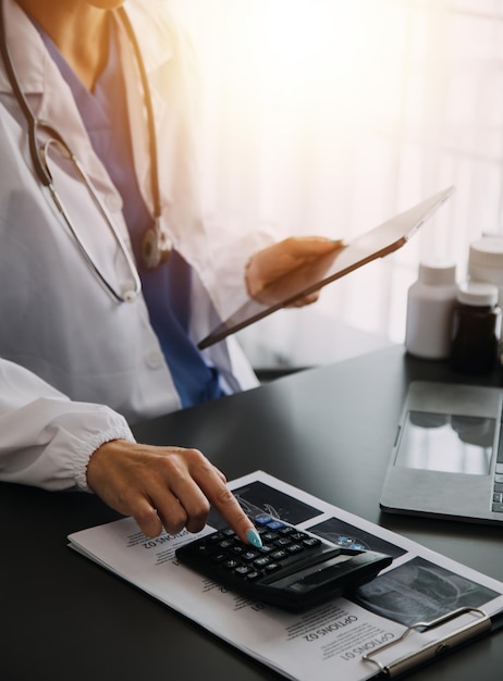 Médico trabalhando com computador portátil e escrevendo em papelada Fundo do hospital