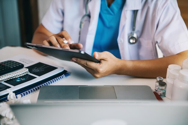 Médico trabalhando em tablet escrevendo prancheta de prescrição com pastas de papel de informações de registro na mesa na clínica Cuidados de saúde e conceito médico
