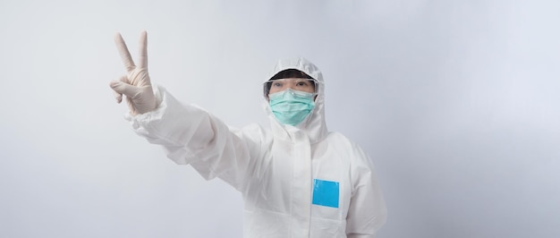 Médico con traje de ppe con guantes de goma médicos blancos y gafas transparentes y mascarilla verde n95 para proteger el gesto del coronavirus pandémico hacer el signo de la mano representar la victoria sobre el virus aislado