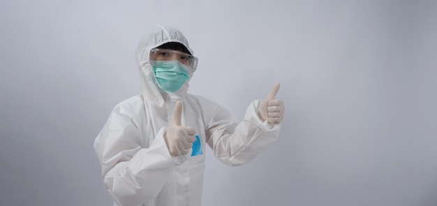 Médico con traje de PPE con guantes de goma médicos blancos y gafas transparentes y mascarilla verde N95 para proteger el gesto del coronavirus pandémico hacer el signo de la mano Representar la victoria sobre el virus Aislado