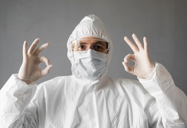 El médico con traje de protección blanco, máscara médica y guantes de goma está mostrando que todo está bien.