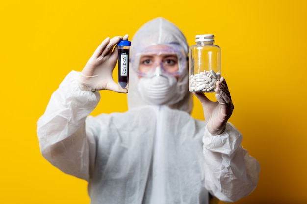 Foto médico en traje de protección y máscara sostiene frascos con pastillas y sangre