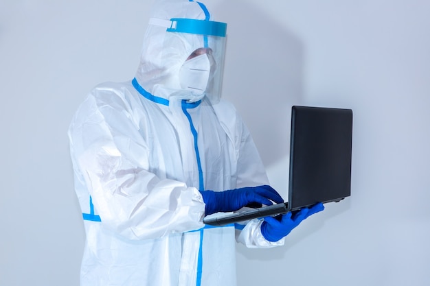 Médico con traje de protección médica, gafas, máscara y guantes trabajando en una computadora portátil. Protección mers por epidemia de virus. Coronavirus (COVID-19). Concepto de salud.